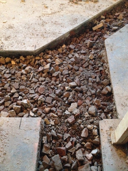 A cut-out in the floor for drain pipe placement. The rubble is evidence of other buildings that previously occupied this site.