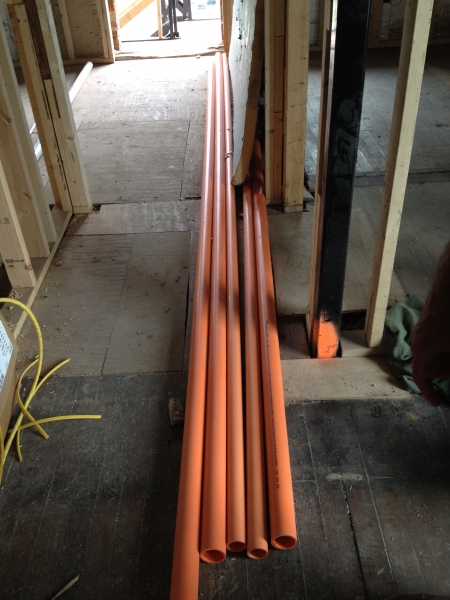 The orange pipe is part of the fire suppression supply lines.  It carries water to concealed sprinkler heads that will be through the building.