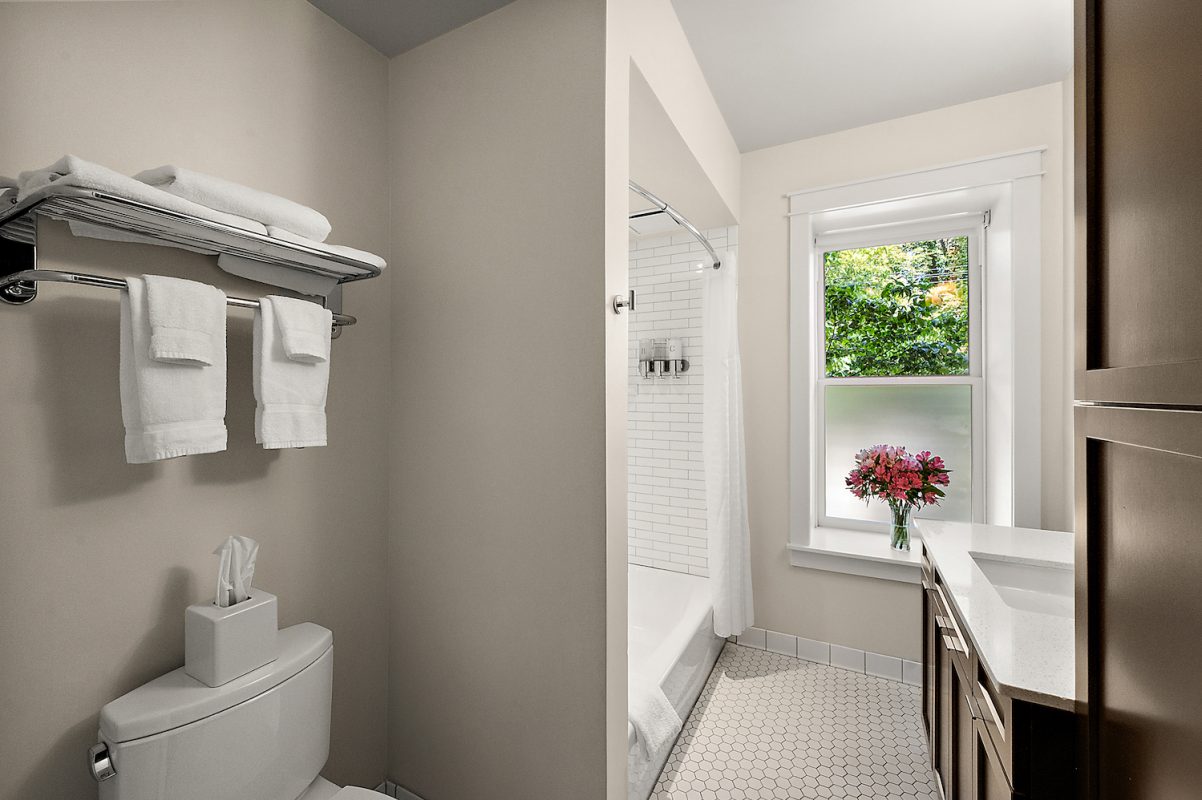 The modern Moore Suite bathroom featuring a sink, mirror, and a window with a bouquet of flowers.